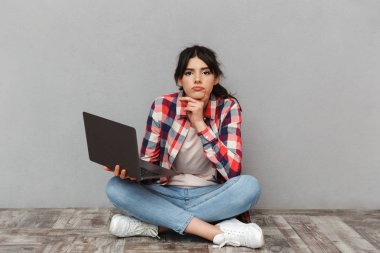 Dizüstü bilgisayar kullanan gri arka plan duvardan izole üzgün memnun genç bayan öğrenci görüntüsünü.