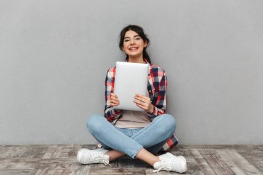 Mutlu genç bayan öğrenci dizüstü bilgisayar tutan gri arka plan duvardan izole görüntüsünü.
