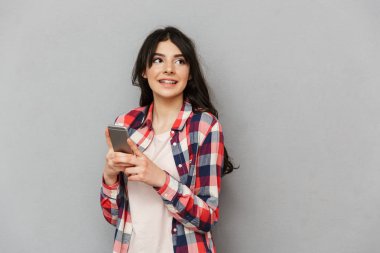 Cep telefonu kullaranarak gri arka plan duvardan izole neşeli genç bayan öğrenci görüntüsünü.