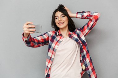 Cep telefonuyla selfie yapmak imge-in sevimli güzel genç bayan gri arka plan duvardan izole.