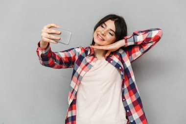 Cep telefonuyla selfie yapmak imge-in sevimli güzel genç bayan gri arka plan duvardan izole.