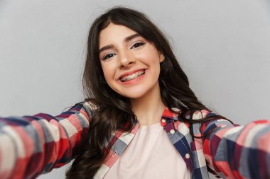 Selfie kamera seyir yapmak imge-in sevimli güzel genç bayan gri arka plan duvardan izole.