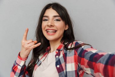 Selfie görünümlü kamera rock jest yapmak yapmak imge-in sevimli güzel genç bayan gri arka plan duvardan izole.