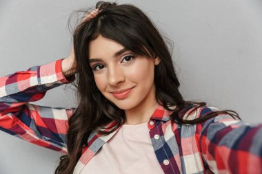 Selfie kamera seyir yapmak imge-in sevimli güzel genç bayan gri arka plan duvardan izole.