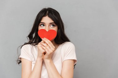 Oldukça genç bayan gri arka plan duvardan izole kalp ile yüz kapsayan görüntüsünü.