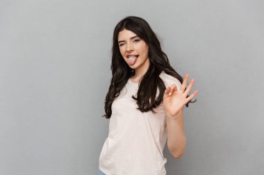 Duygusal güzel genç Bayan iyi jest gösterilen gri arka plan duvardan izole ayakta görüntüsünü.