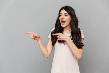 Duygusal güzel genç bayan gri arka plan duvar işaret içinde izole ayakta görüntüsünü.