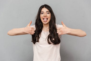 Başparmak yukarıya jest yapmak imge-in duygusal güzel genç bayan gri arka plan duvardan izole ayakta.