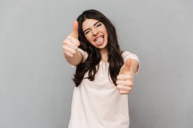 Başparmak yukarıya jest yapmak imge-in duygusal güzel genç bayan gri arka plan duvardan izole ayakta.
