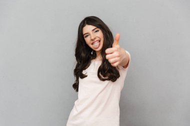 Başparmak yukarıya jest yapmak imge-in duygusal güzel genç bayan gri arka plan duvardan izole ayakta.