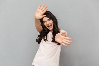 Sevimli güzel genç bayan için sallayarak gri arka plan duvar üzerinde izole ayakta görüntüsünü.