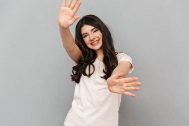 Sevimli güzel genç bayan için sallayarak gri arka plan duvar üzerinde izole ayakta görüntüsünü.