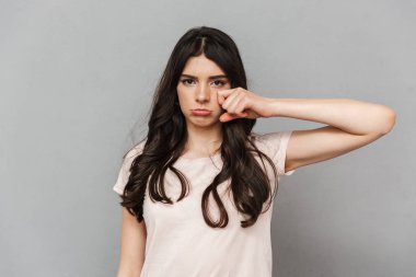 Memnun üzgün genç bayan gri arka plan duvardan izole ayakta görüntüsünü.