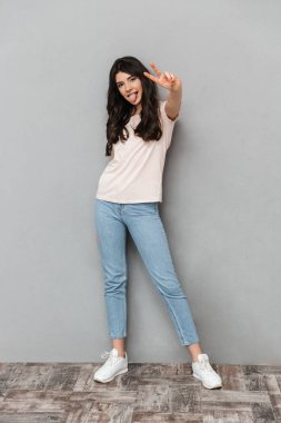 Çok hoş genç bayan barış hareketi gösterilen gri arka plan duvardan izole ayakta fotoğrafı.