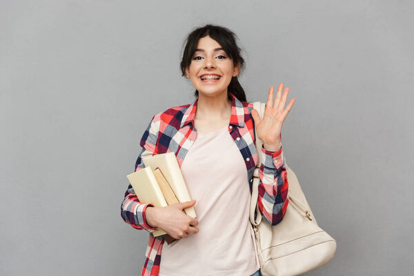 Image of happy young lady student standing isolated over grey background wall holding books.