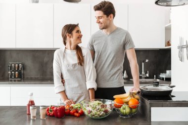 Gülümseyen genç bir çift birlikte mutfakta yemek portresi