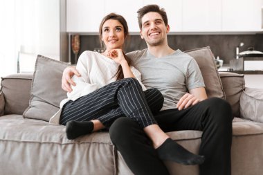 Gülümseyen genç bir çift Tv izlerken evde bir kanepede rahatlatıcı portresi