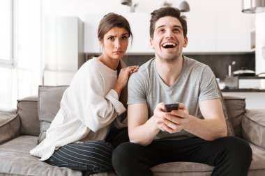 Tv izlerken erkek arkadaşıyla bir kanepede oturan üzgün bir genç kadın portresi