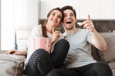 Bir genç çift Tv izliyor ve patlamış mısır yemek sırasında evde bir kanepede rahatlatıcı portresi