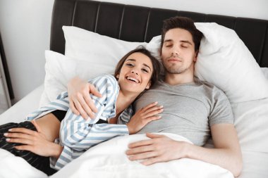 Birlikte yatakta yatan genç gülümseyen bir çift portresi