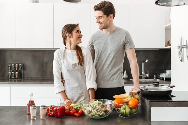 Gülümseyen genç bir çift birlikte mutfakta yemek portresi