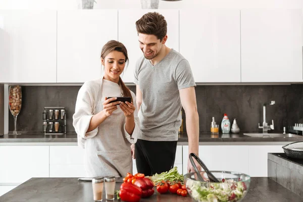 Retrato Jovem Casal Sorrindo Cozinhando Juntos Cozinha Usando Telefone Celular — Fotografia de Stock