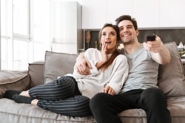 自宅のテレビを見ながらソファでくつろいで幸せな若いカップルの肖像画 — ストック写真