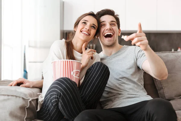 自宅のソファでテレビを見ながらポップコーンを食べてリラックス陽気な若いカップルの肖像画 — ストック写真