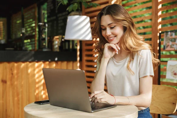 Oturma ve bir kafe açık havada dizüstü bilgisayar kullanan genç ve güzel bir kız portresi