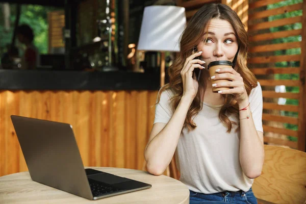 Dizüstü bilgisayar ile oturan ve bir kafe açık havada kahve içme sırasında cep telefonu üzerinde konuşurken bir genç ve güzel kız portresi