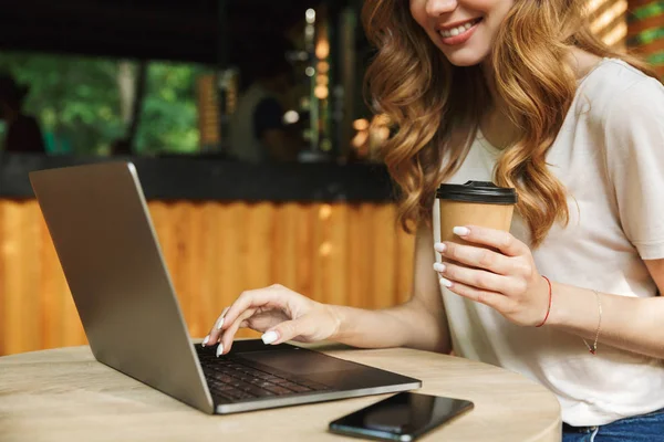 Dizüstü bilgisayarda yazarak ve kahve Kupası'nda tablo açık havada tutan bir gülümseyen kadın kapatmak