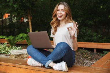 Dizüstü bilgisayar üzerinde bir tezgah açık havada oturma ve ok gösterilen süre kullanan genç kız gülümseyerek