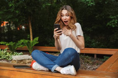 Bir tezgah açık havada üzerinde otururken cep telefonu kullanan sürpriz genç kız