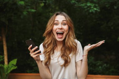 Bir tezgah açık havada üzerinde otururken cep telefonu tutan genç kız heyecanlı