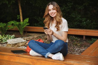 Bir tezgah açık havada üzerinde otururken cep telefonu kullanan genç kız gülümseyerek