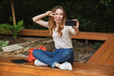 Bir tezgah açık havada üzerinde otururken selfie alarak oynak genç kız