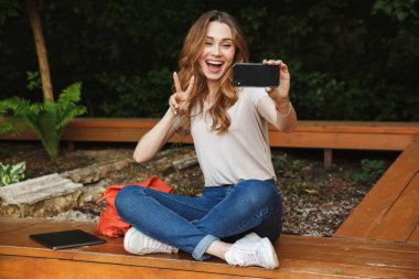 Bir bankta açık havada oturma ve barış hareketi gösterilen selfie alarak mutlu genç kız