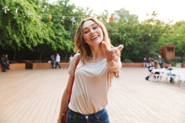 Gülümseyen genç kadın ile sırt çantası ayakta açık havada outsretched el ile