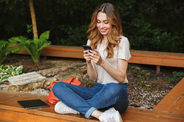 Bir tezgah açık havada üzerinde otururken cep telefonu kullanan genç kız gülümseyerek