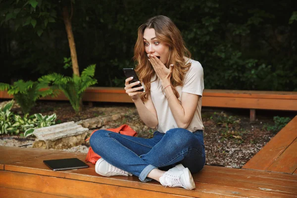 Bir tezgah açık havada üzerinde otururken cep telefonu kullanan sürpriz genç kız