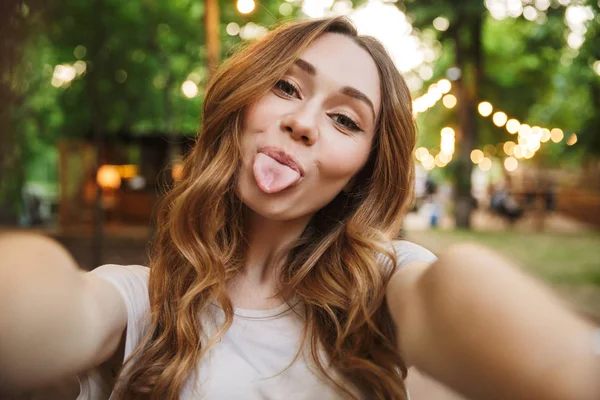 Close up of funny young girl taking a selfie with outstretched hand while standing at the park