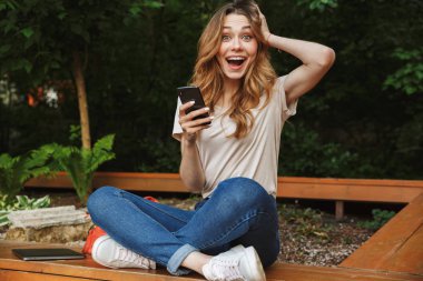 Bir tezgah açık havada üzerinde otururken cep telefonu kullanan genç kız heyecanlı