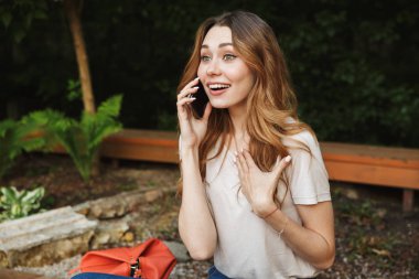 Genç kız açık havada bankta otururken cep telefonu üzerinde konuşurken gülümseyen