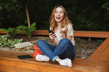 Bir tezgah açık havada üzerinde otururken cep telefonu kullanan memnun genç kız