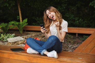 Bir tezgah açık havada üzerinde otururken cep telefonu kullanan neşeli genç kız