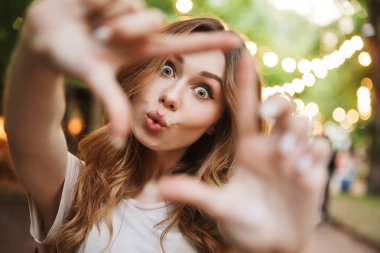 Neşeli genç kız gösteren çerçevesi parmak parkta duran yakın çekim