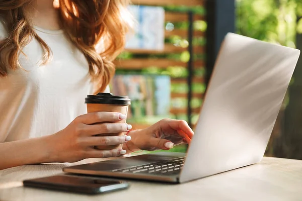 テーブルにラップトップ コンピューターに入力し 屋外でのコーヒーのカップを保持している女性のクローズ アップ — ストック写真