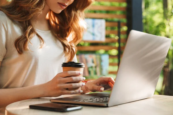 Dizüstü bilgisayarda yazarak ve kahve Kupası'nda tablo açık havada tutan bir kadının yakın çekim