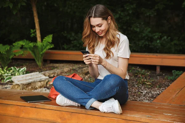 Bir tezgah açık havada üzerinde otururken cep telefonu kullanan güzel genç kız