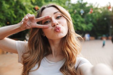 Genç ve güzel bir kız açık havada selfie uzanmış el ile alarak ve barış hareketi gösterilen yakın çekim